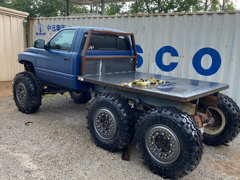 Rear three-quarter view of the blue Ram 6x6 showing the steel flatbed and both rear Rockwell axles with their links